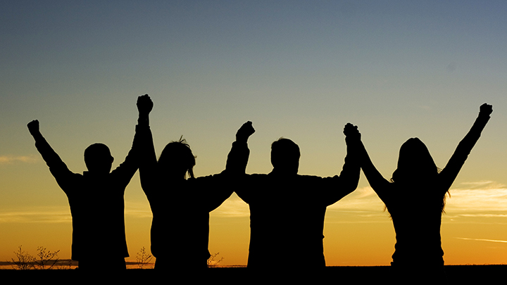 silhouette of four people holding hands with arms lifted up