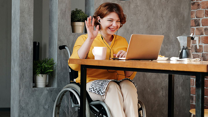 woman sitting in wheelchair waving at laptop while on video call