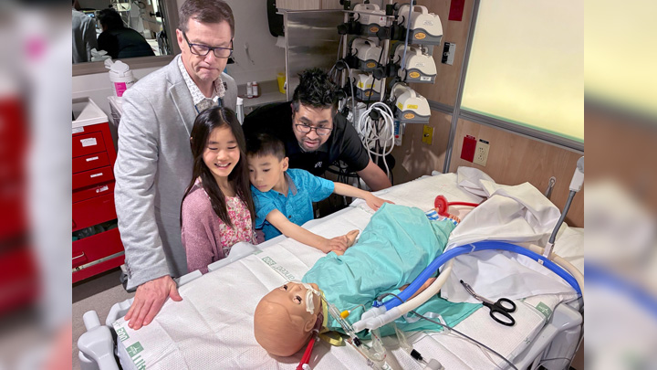 Dr. Laurance Lequier, left, ECLS program medical director, and Archie Enano, ECLS educator, show James and Izzy the simulation doll used for ECMO training.