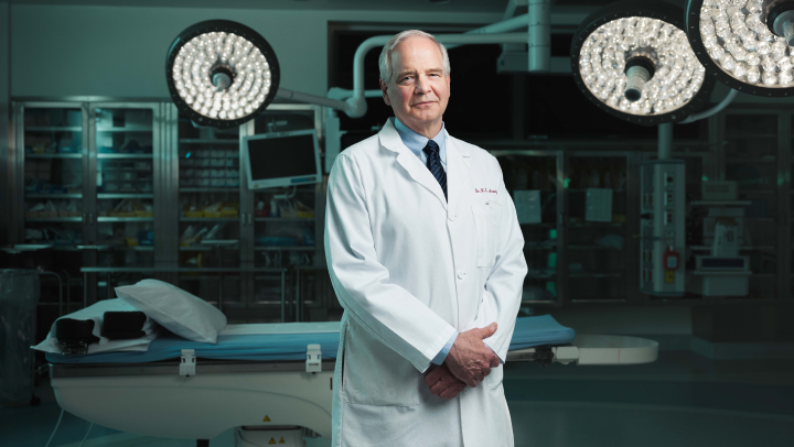 Photo of a doctor, Dr. Keith Aronyk, in a lab coat standing in an operating room
