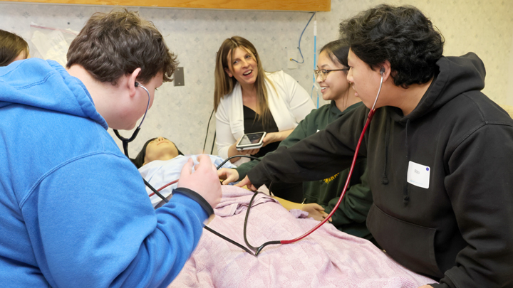 people with stethoscopes sit around a mannequin