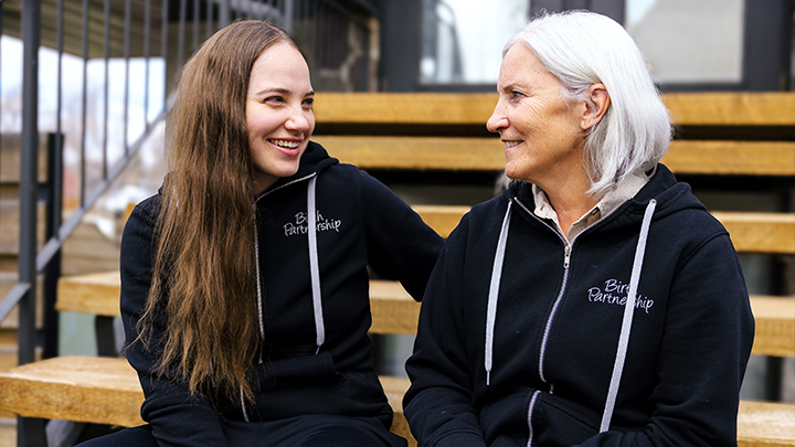 Registered midwives Sadie Lenstra, left, and her mom Patty pose on the steps of the Birth Partnership Midwifery Services clinic in Calgary. “I truly burst with pride every time I get to work with Sadie,” says Patty. “Together, she and I share a passion for the care we provide to our families — and we share it deeply.”