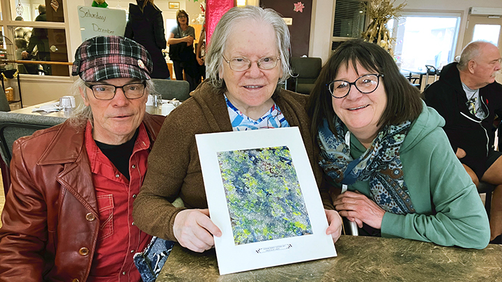 Artist Linda Rice, centre, is joined by her son Terry, left, and his wife Maggie Taylor as she shows off her favourite artwork that she created for the Opening Minds through Art silent auction.