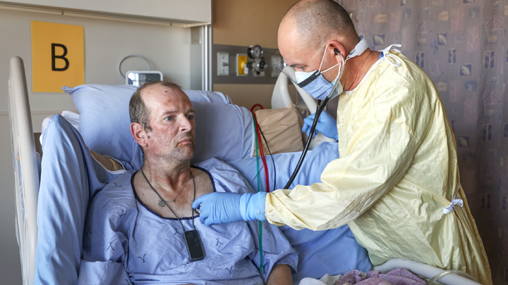 A member of the healthcare team listens to the lungs of patient Tracey Barclay. Barclay tested positive for COVID-19, and now plans to get the vaccine just as soon as he’s able.