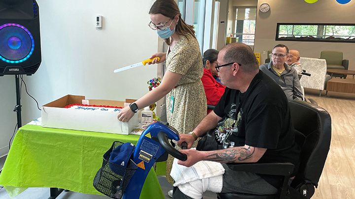 Recreation therapist Tiffany Sceviour cuts a cake for Willow Square Continuing Care Centre resident Glen Docherty earlier this summer. Staff and residents celebrated the one-year anniversary of the Willow Square Continuing Care Centre.