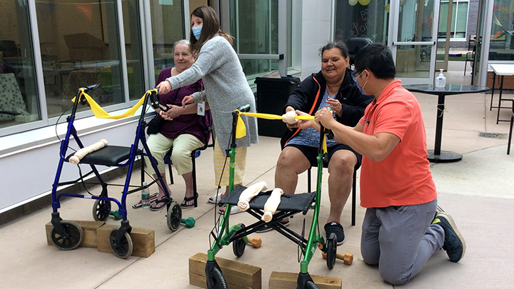 Willow Square Continuing Care Centre residents Grace Wanderingspirit and Patricia Gabriel participate in a slingshot target practice game, with the assistance of AHS social work student Susan Greening and occupational therapist Kent Tsui.